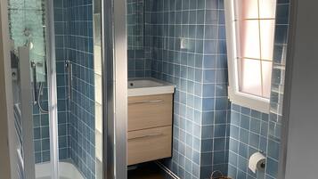 Een badkamer met een douchecabine, toilet, wastafel en een raam.