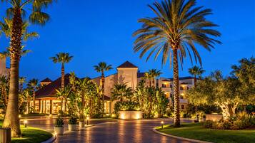 A resort with palm trees, a paved walkway, and buildings with warm lighting.