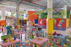 Un espace de jeux intérieur coloré, équipé de tables, de chaises et de structures ludiques.