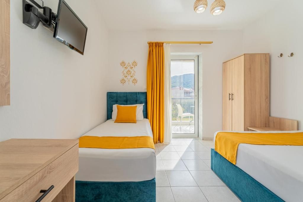 Habitación de hotel con dos camas, televisión montada en la pared, armario y balcón con cortinas.