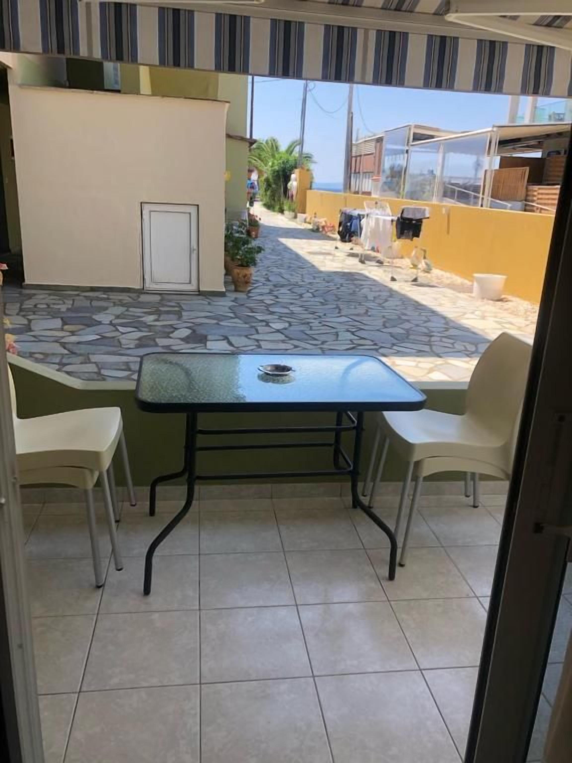 A patio with a table and chairs, a door, and a view of a street with buildings and a palm tree.