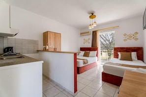 A compact hotel room with a kitchenette, two beds, a small dining area, and a view of the outdoors. - Chrissi Ammoudia (Toroni)