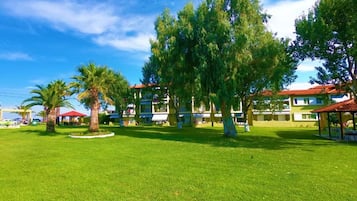 A hotel courtyard with a well-maintained lawn, several trees, and a building with a red roof in the background.