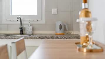 Una cocina con un lavamanos, un hervidor y una botella sobre la encimera.