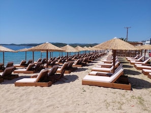 A beach with rows of sun loungers and thatched umbrellas. - Chrissi Ammoudia (Toroni)