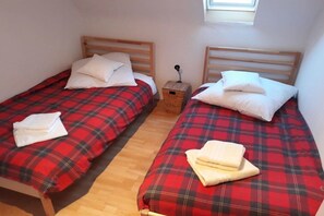 A room with two single beds, each with a red and black checkered bedspread and white pillows. There is a small wooden nightstand between the beds with a lamp on it. - Holiday apartment with 2 bedrooms (Simmerath)