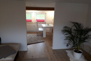 A room with a wooden floor, a white radiator, a white table with a plant, and a window with red blinds. - Holiday apartment with 2 bedrooms (Simmerath)