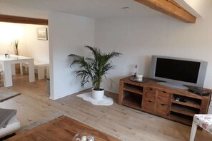 A living room with a TV, wooden entertainment unit, a potted plant, and a white sofa. - Holiday apartment with 2 bedrooms (Simmerath)