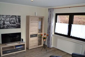 A living room with a television, wooden cabinet, and a window with curtains. - Mountain idyll by the lake (Winterberg- Niedersfeld)