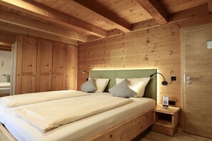 Ein Zimmer mit Holzboden, einem Bett, einem Nachttisch und einer Tür.