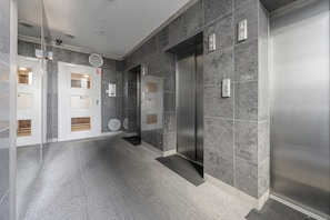 A modern elevator with a metallic finish, adjacent to a door with a window and a control panel. - Lumina 2BR Apt w/ Parking & Balcony & AC (Warszawa)