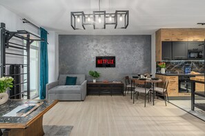 A modern living room with a grey sofa, a coffee table, and a dining area with a wooden table and chairs. - Lumina 2BR Apt w/ Parking & Balcony & AC (Warszawa)