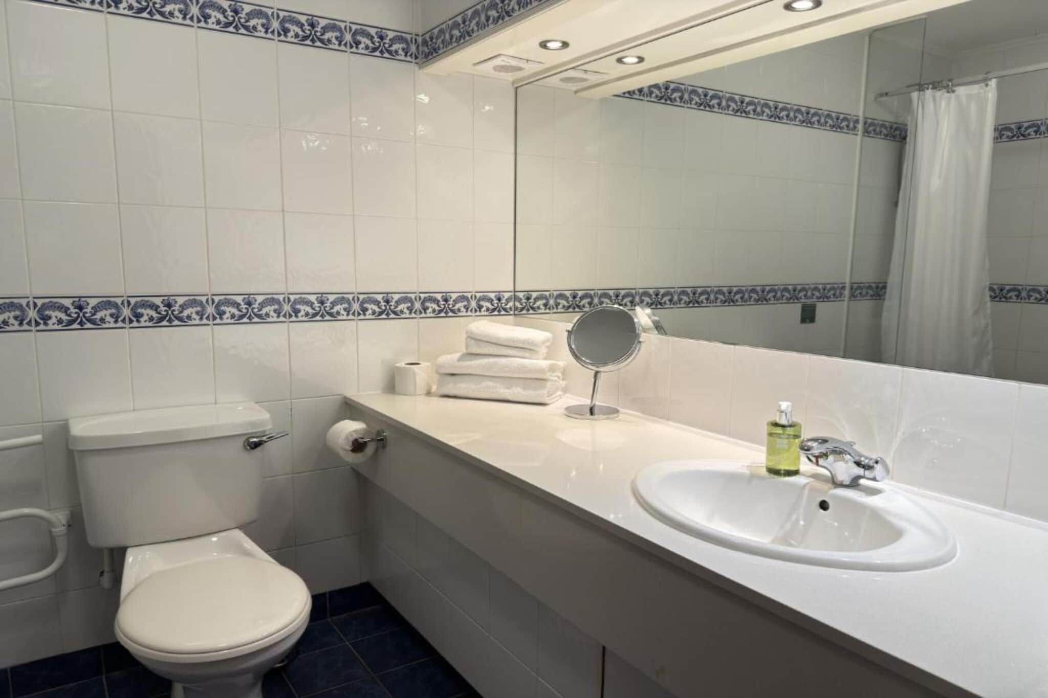 Et badeværelse med toilet, vask og spejl.