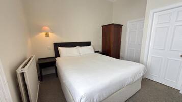 A bedroom with a bed, a nightstand, a wall-mounted lamp, a wardrobe, and a door.