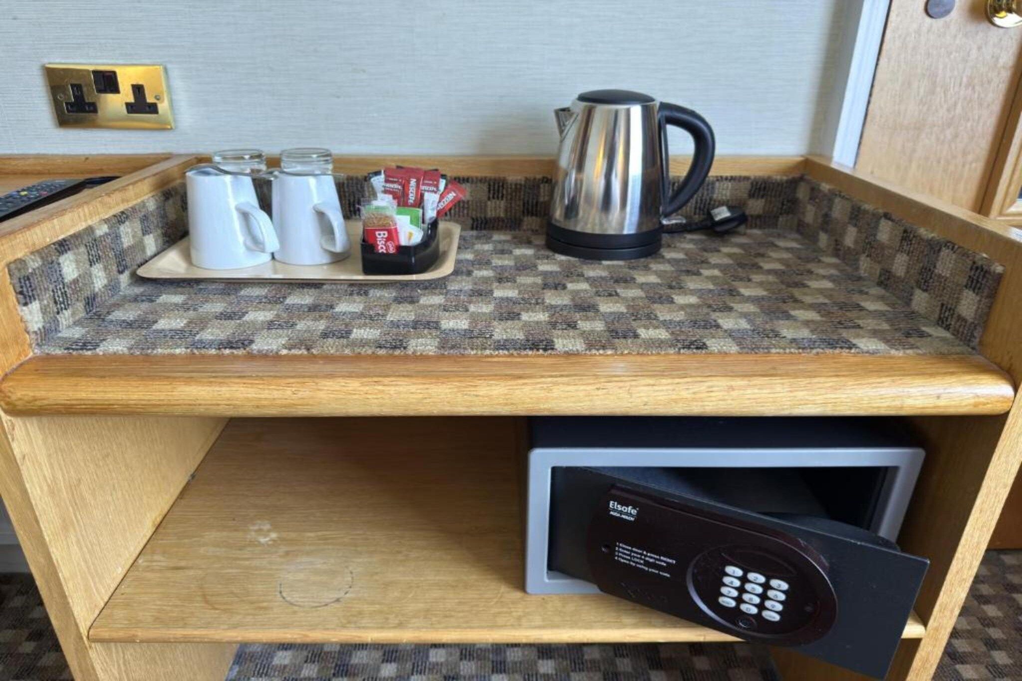 A kitchenette with a coffee maker, tea pots, and a kettle on a checkered countertop.