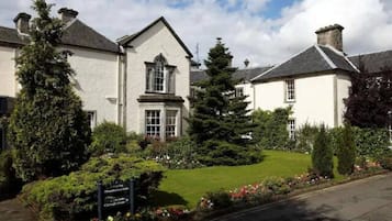 A two-story building with a symmetrical facade, a central entrance with a window, and a well-maintained garden with a variety of shrubs and flowers.