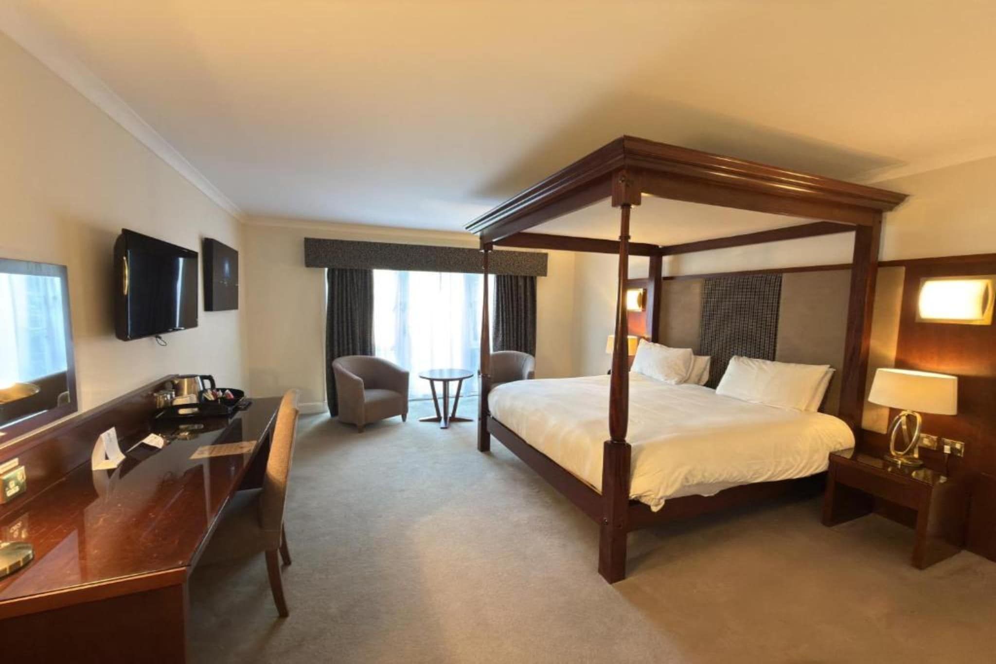 Ein Hotelzimmer mit Himmelbett, Schreibtisch mit Stuhl, Fernseher und einem kleinen Tisch mit Sitzgelegenheit.