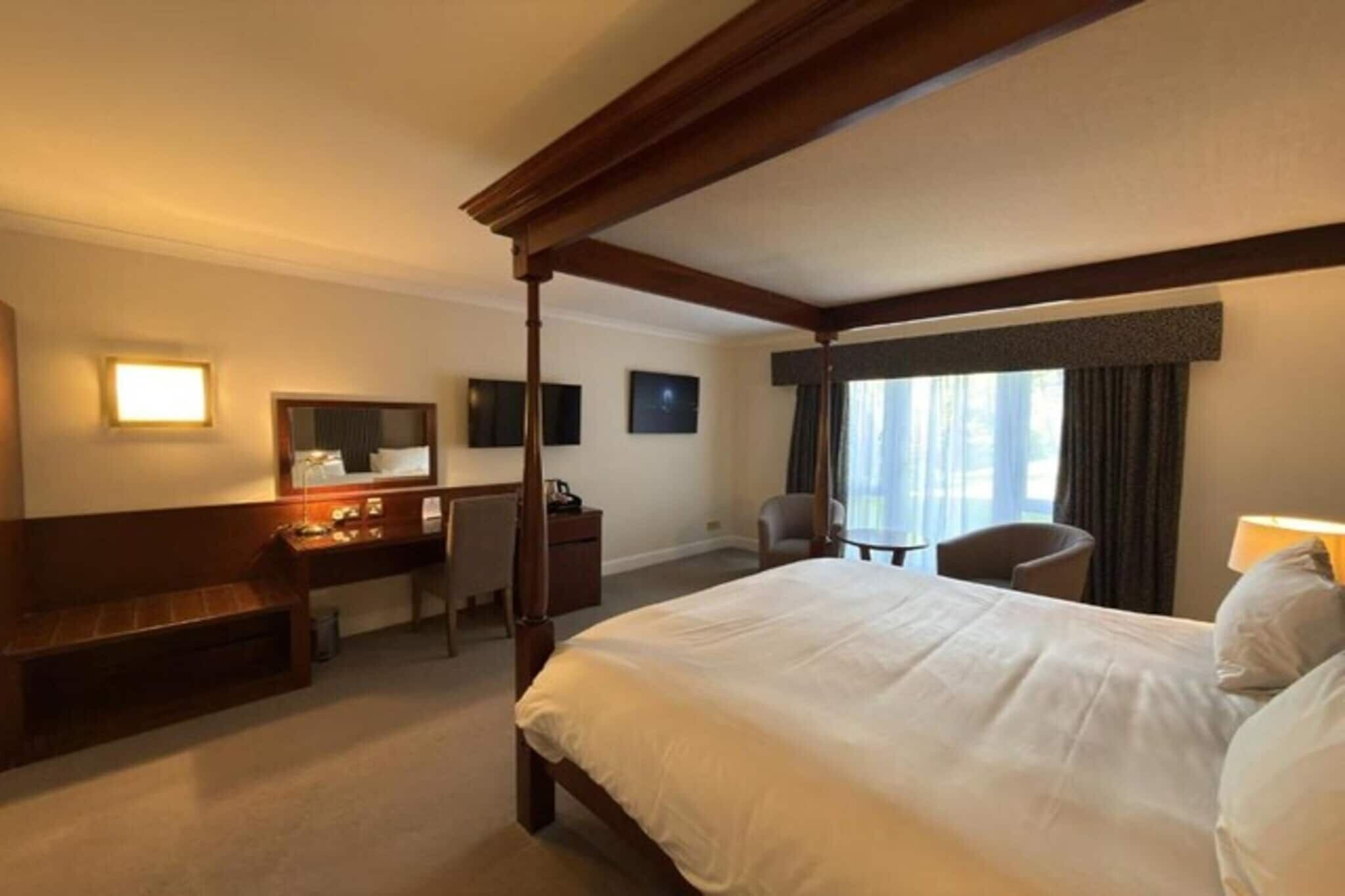 Ett hotellrum med en säng med himmelssäng, ett skrivbord, en stol, en tv och ett fönster med gardiner.