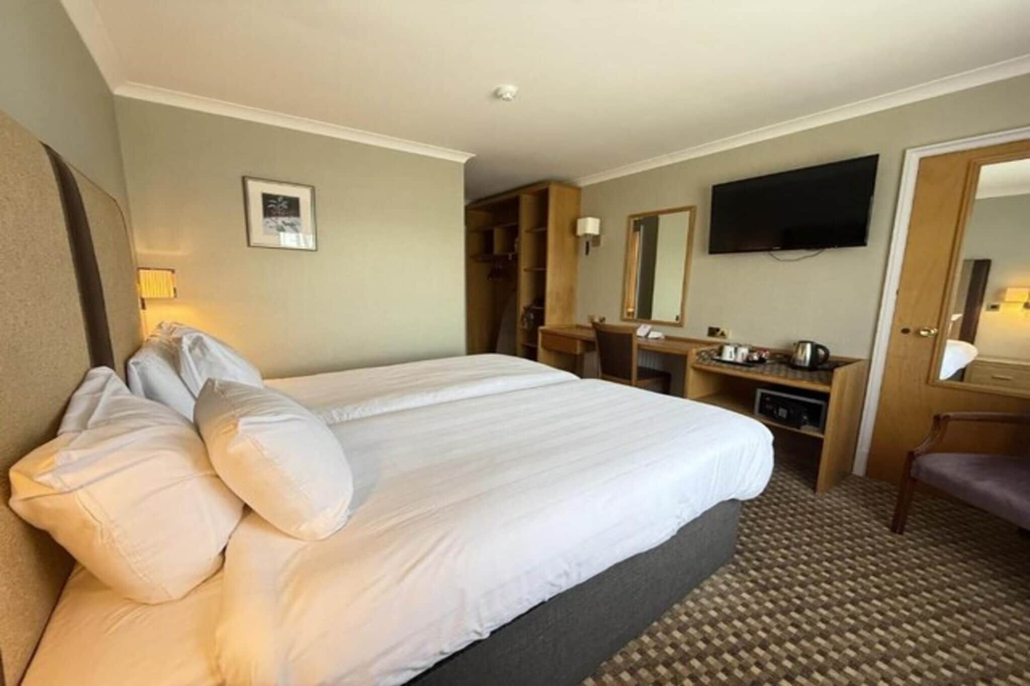 Una habitación de hotel con una cama grande, un escritorio, una silla, un televisor y un espejo.