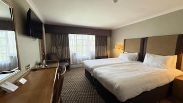 Una habitación de hotel con una cama, un escritorio, una silla, un televisor y un ventanal con cortinas.