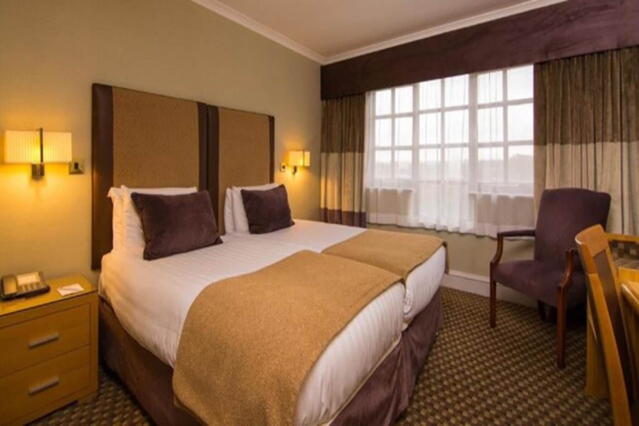 A hotel room with a double bed, a desk, a chair, and a window with curtains.