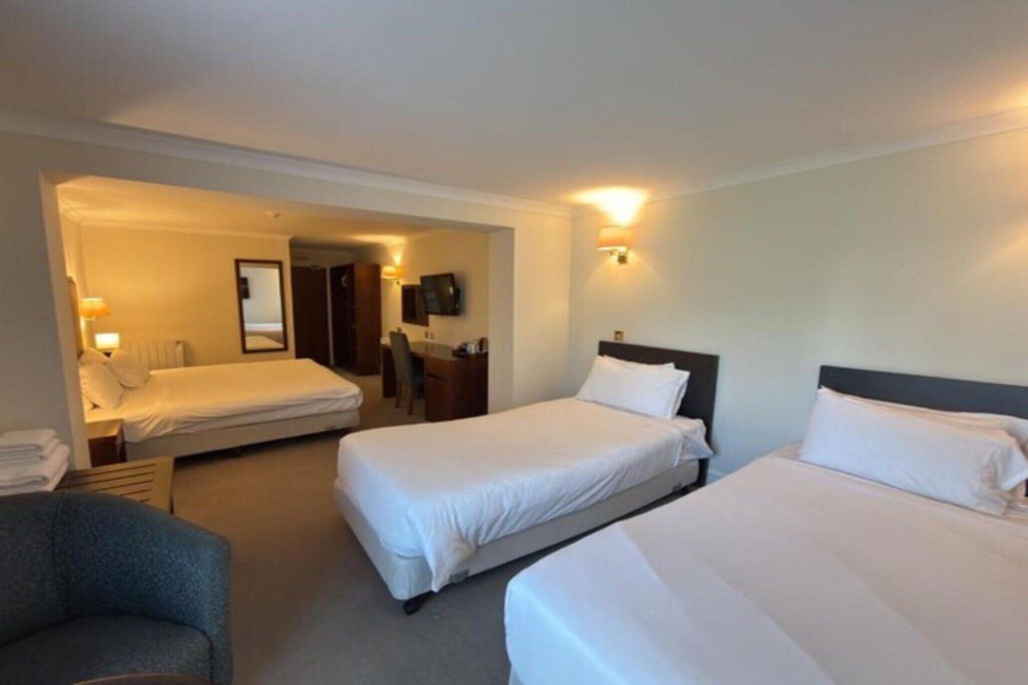 A hotel room with two beds, a desk, a chair, and a television.