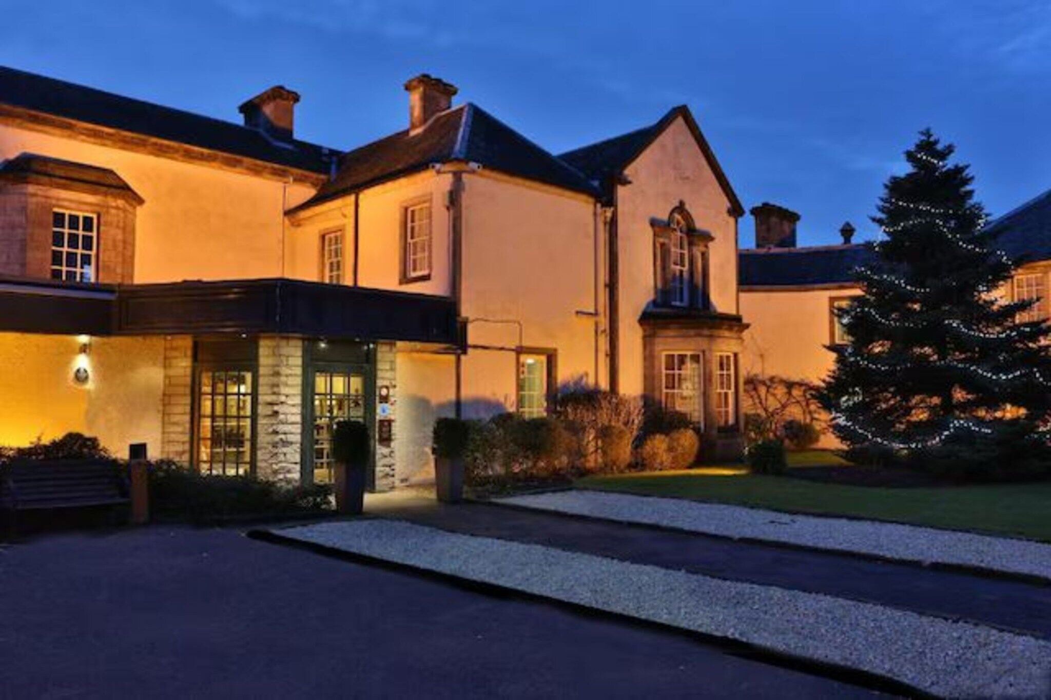 A building with a traditional architectural style, featuring a prominent entrance with a door and windows, and a well-maintained lawn with a Christmas tree.