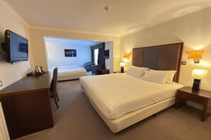 Ein Hotelzimmer mit einem großen Bett, einem Schreibtisch, einem Sessel und einem an der Wand befestigten Fernseher.