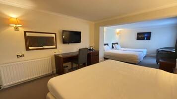 Habitación de hotel con una cama grande, un escritorio, una silla, un televisor y una cama con dos almohadas.