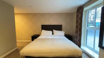 Ein Hotelzimmer mit einem großen Bett, zwei Nachttischen, einer Wand mit Muster und einem Fenster mit Vorhängen.