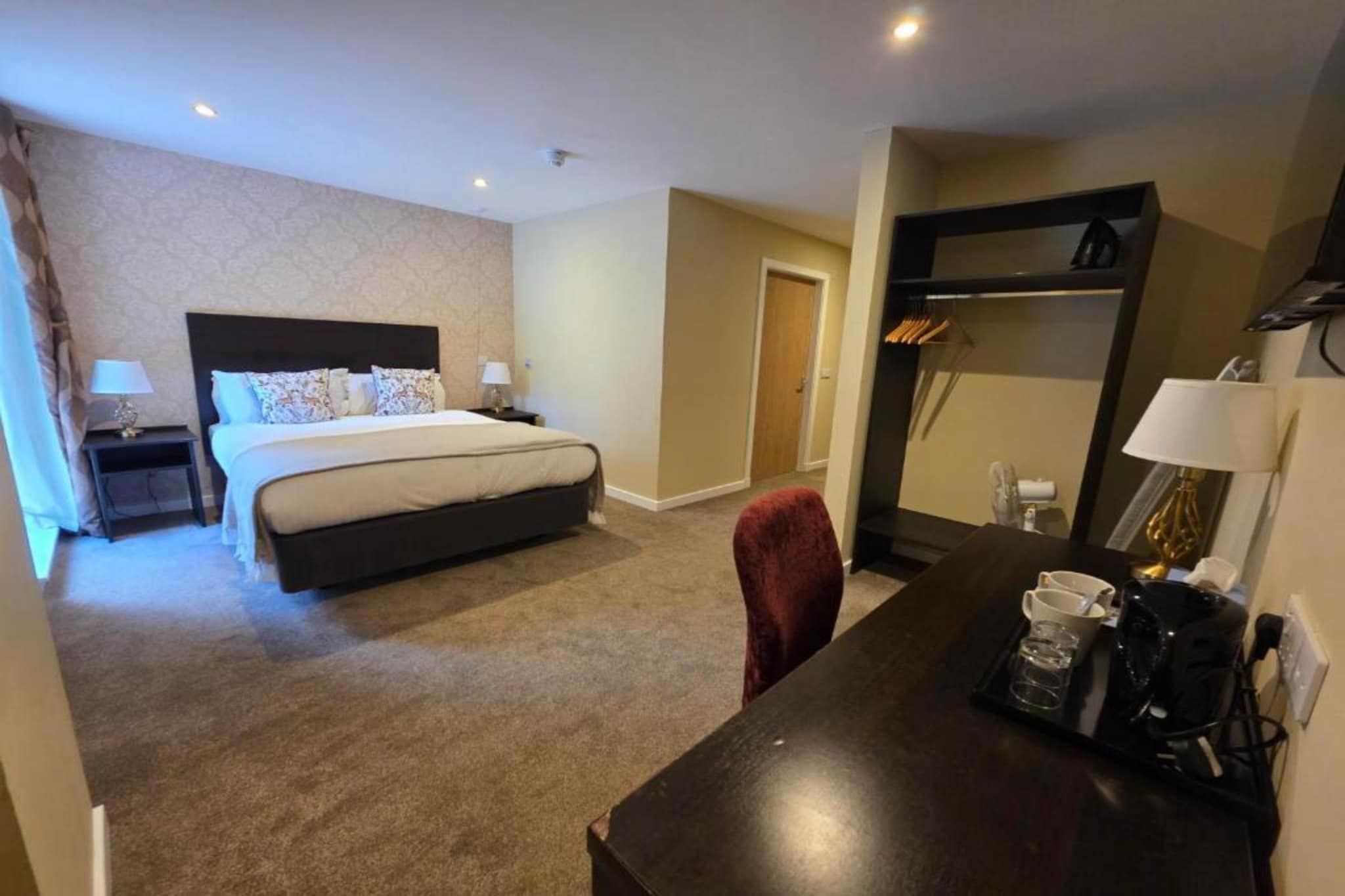 Een hotelkamer met een bed, nachtkastjes, een bureau met koffiezetapparaat en een kledingkast.