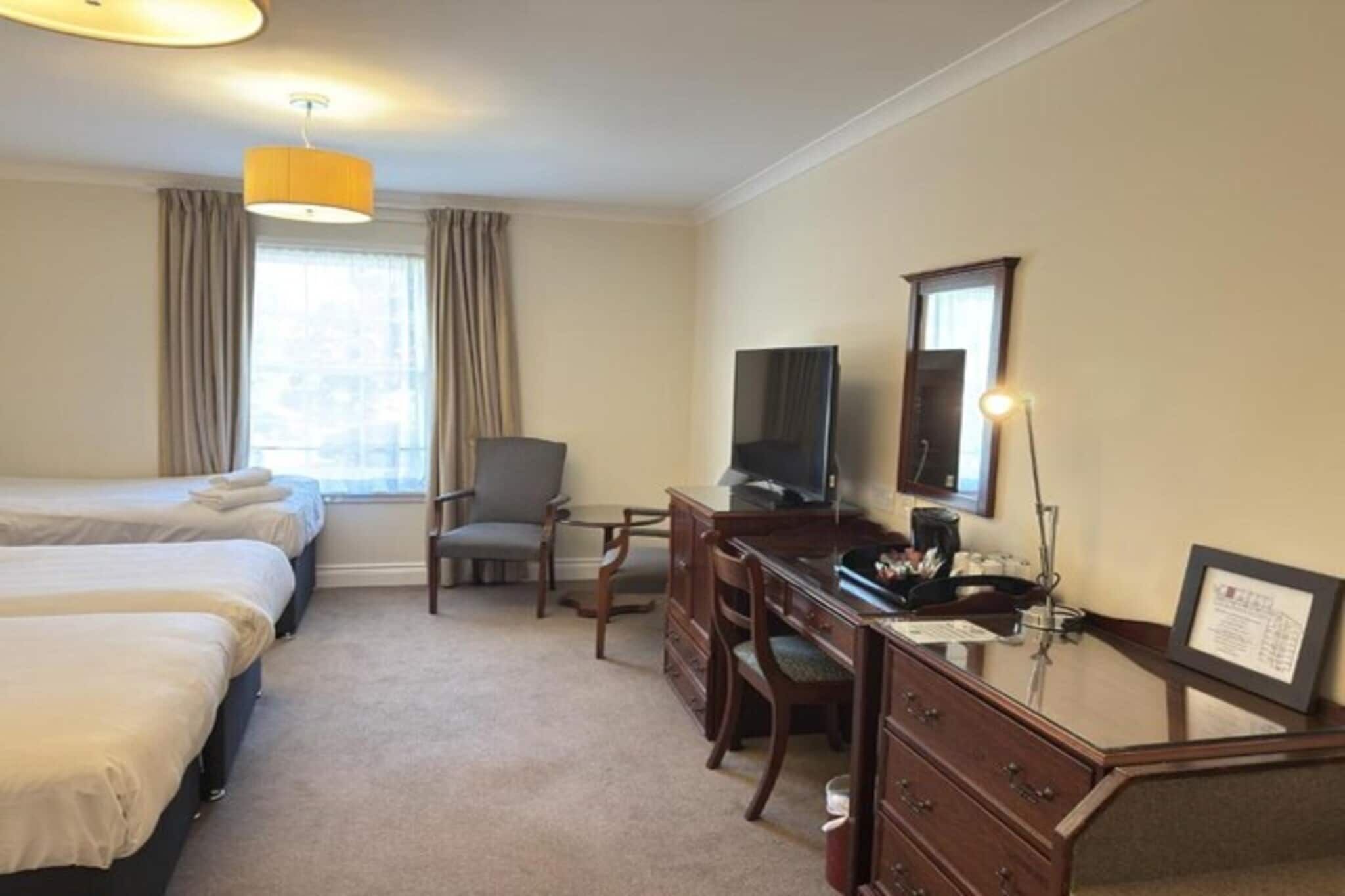 A hotel room with two beds, a desk with a chair, a television, and a window with curtains.