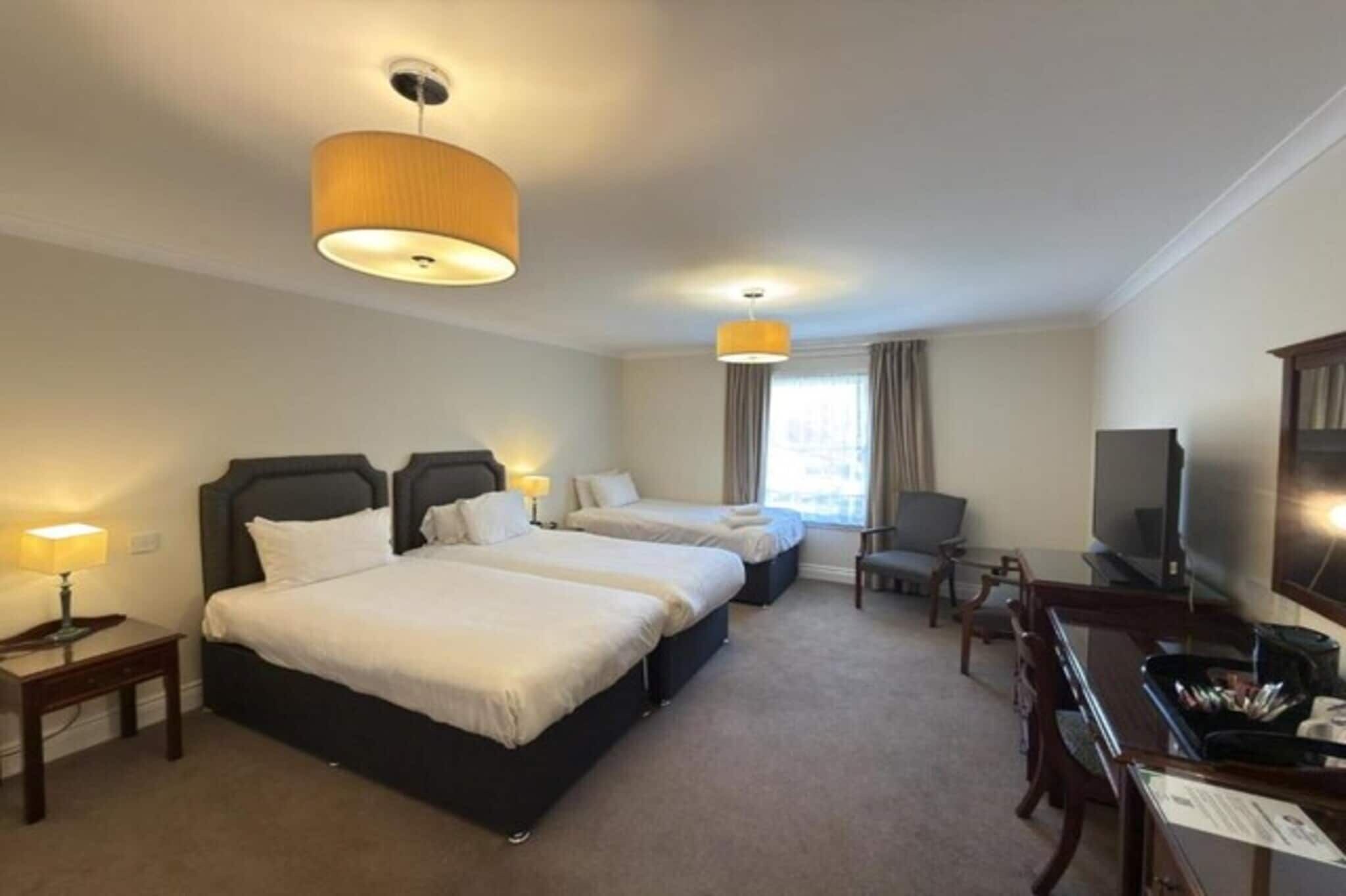 A hotel room with two beds, a desk, a chair, and a television.