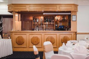 Een bar met houten lambrisering en diverse flessen en glazen.