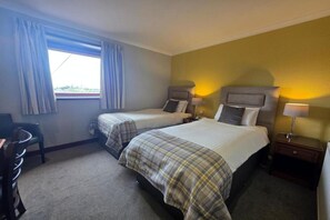 Een hotelkamer met twee bedden, een bureau en een raam met gordijnen.