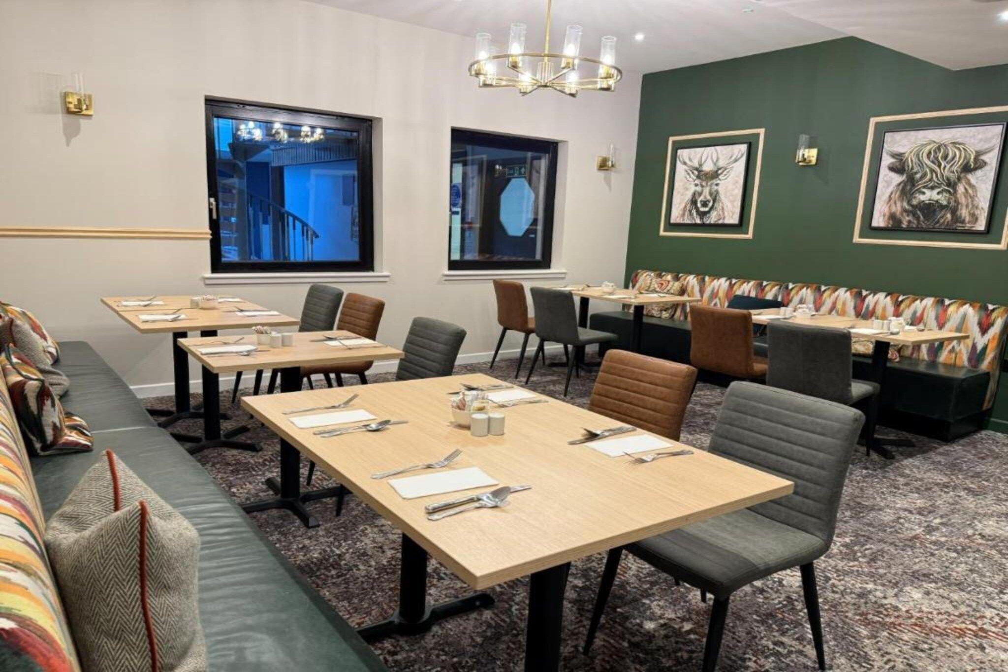 A conference room with long tables, chairs, and a sofa. There are two windows with views of buildings.