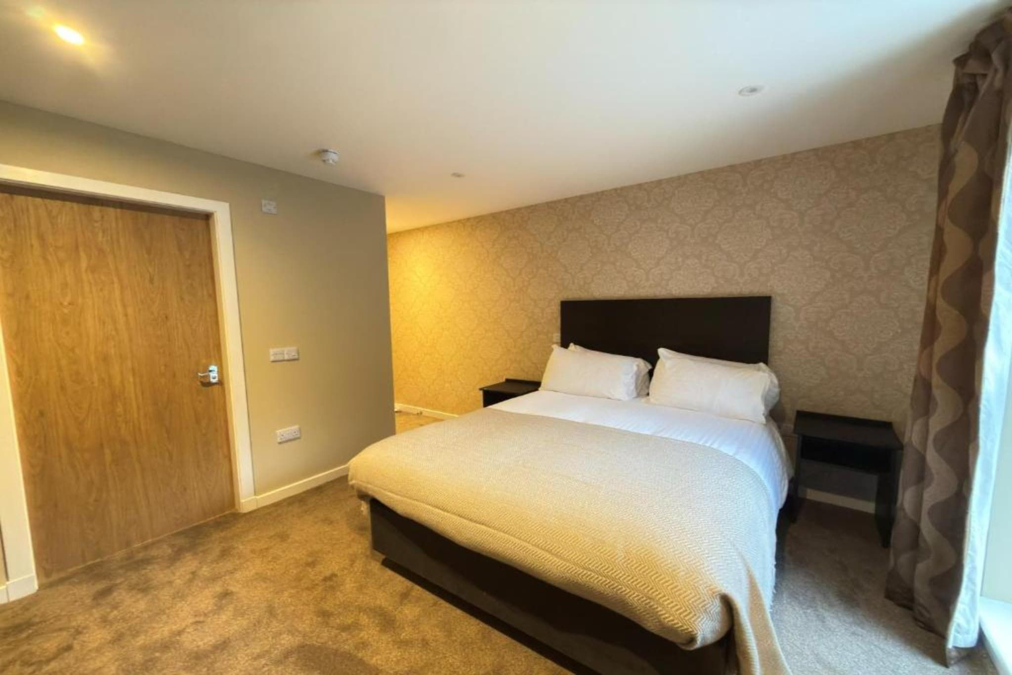 Een hotelkamer met een groot bed, een houten deur en een behang met patroon.