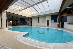 Una piscina interior con techo de vidrio, suelo de baldosas y un cartel de prohibición de saltos.