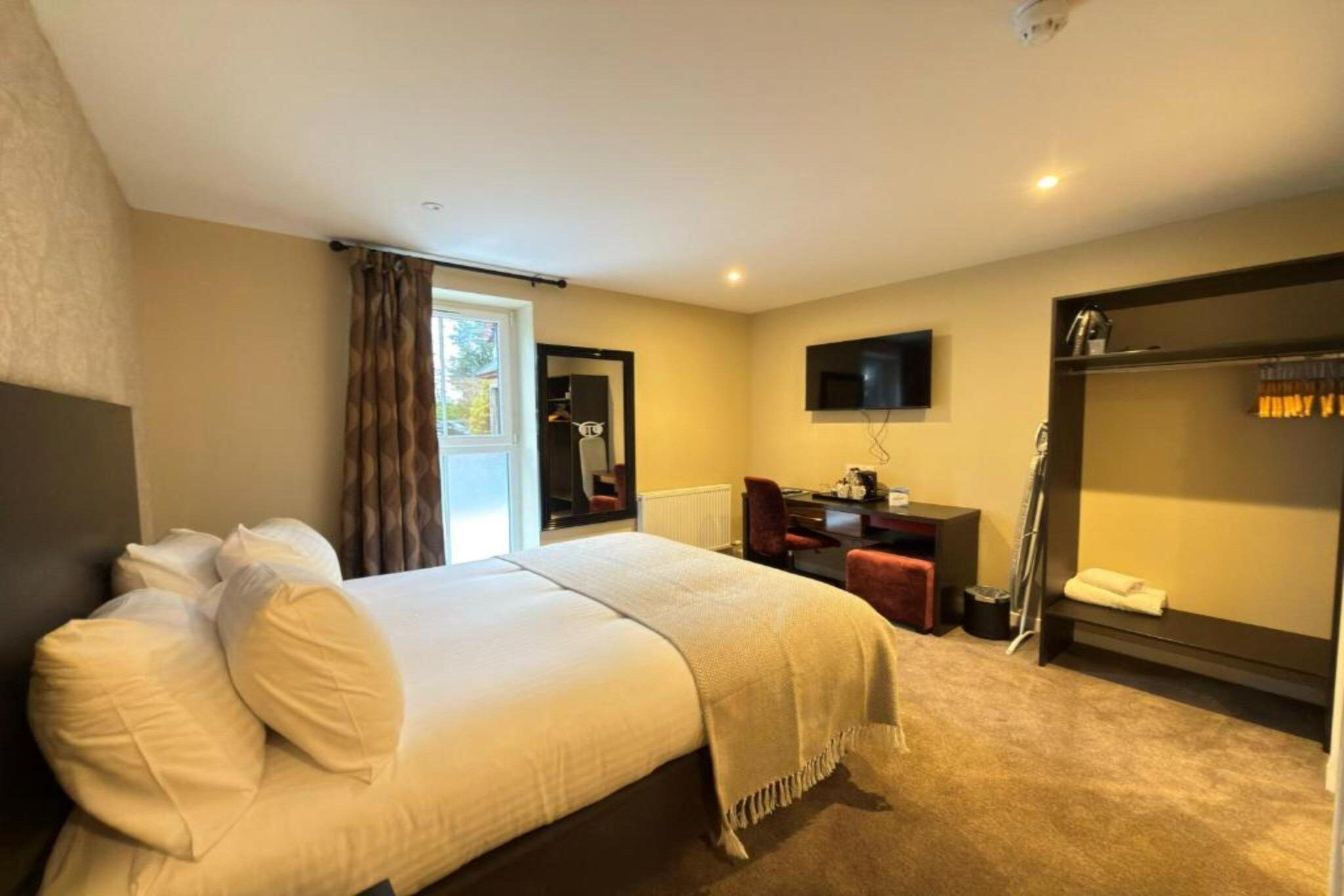 Ein Hotelzimmer mit Bett, Schreibtisch, Fernseher und Kleiderschrank.