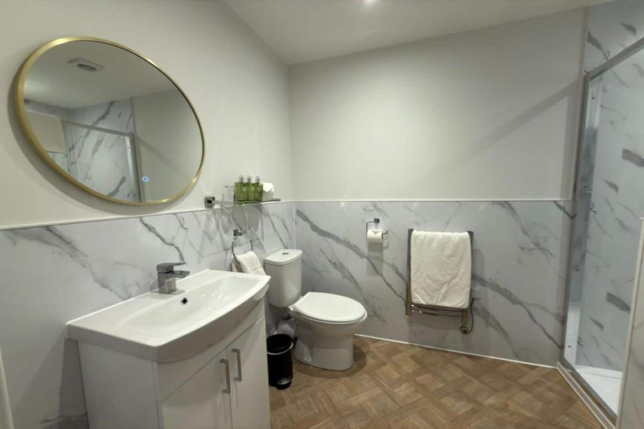Un bagno moderno con parete in marmo, uno specchio rotondo, un lavabo, un water e una zona doccia.
