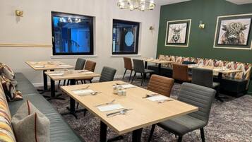 A conference room with long tables, chairs, and a sofa. There are two windows with views of buildings.