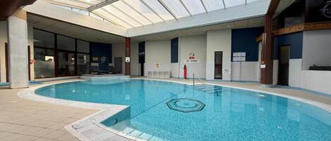An indoor swimming pool with a glass ceiling, tiled floor, and a no diving sign.