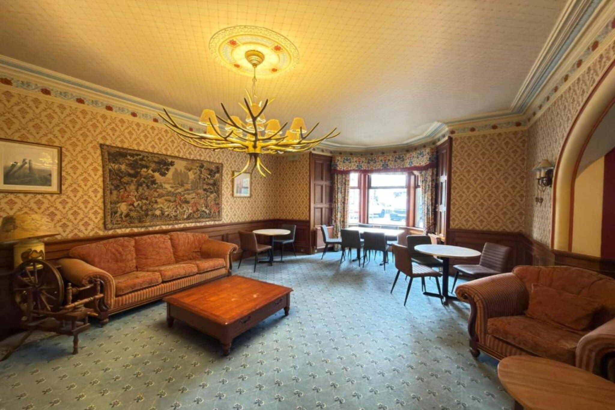A room with a patterned carpet, a sofa, a coffee table, a chandelier, and a painting on the wall.