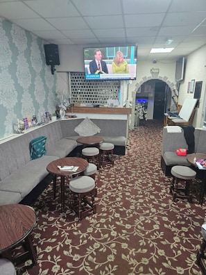 A hotel lobby with a television displaying news, a reception desk, seating area, and a patterned carpet. - charnley gold hotel (Blackpool)