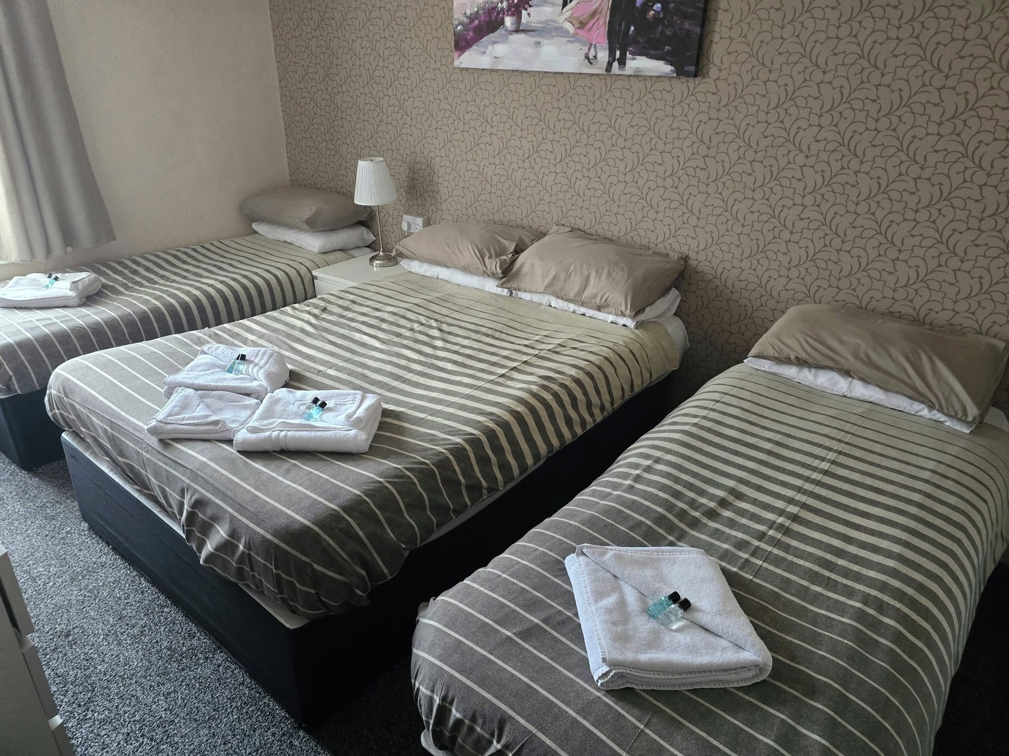 A hotel room with three beds, each with striped bedding and towels.