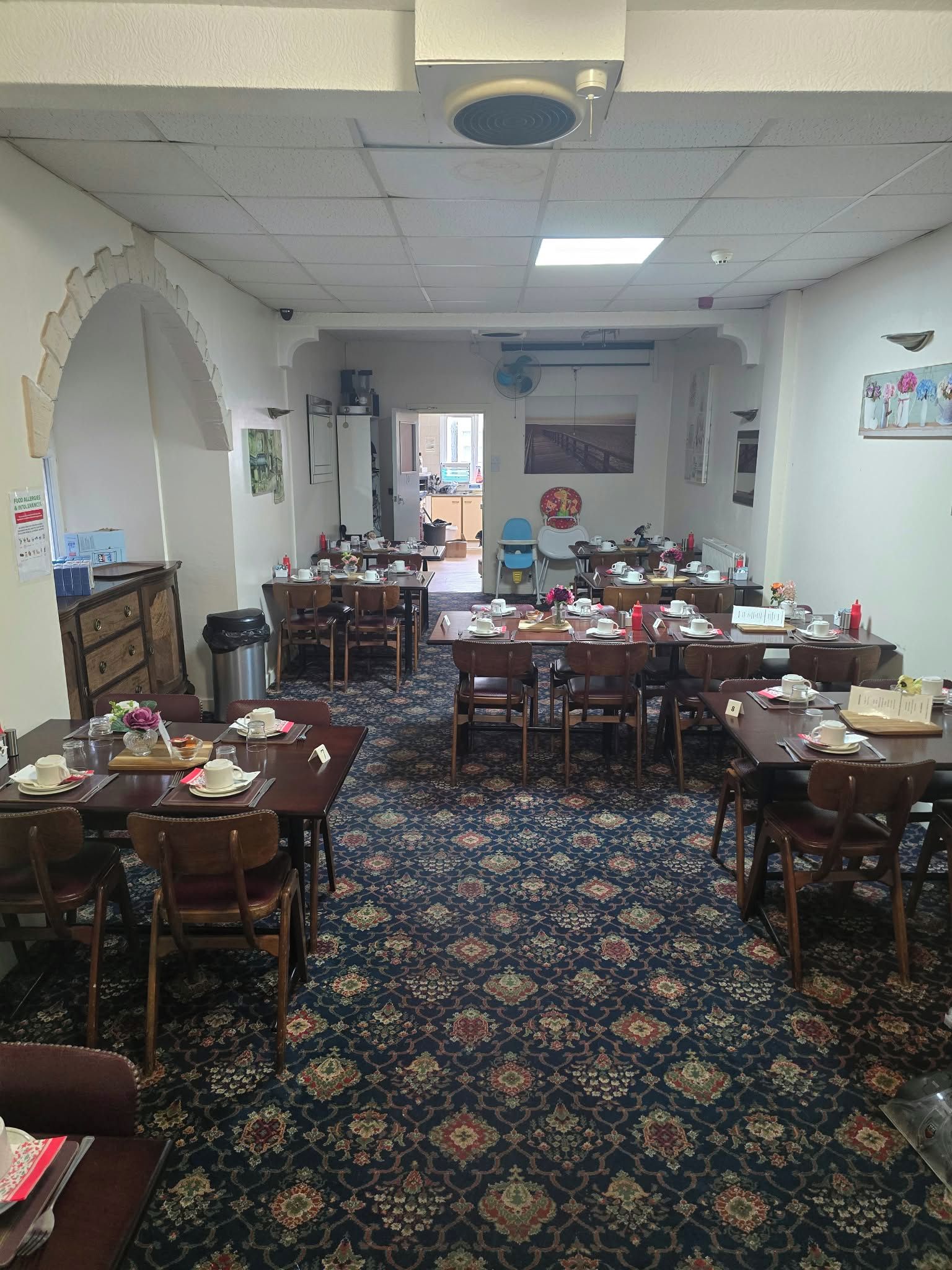 A dining area with multiple tables and chairs, a patterned carpet, and a ceiling fan.
