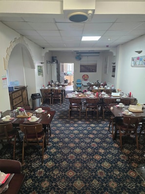 A dining area with multiple tables and chairs, a patterned carpet, and a ceiling fan. - charnley gold hotel (Blackpool)