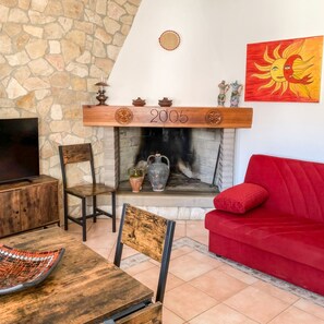 A cozy living room with a stone wall, a fireplace, a red sofa, and a television on a wooden table. - Domo Juanna - Cozy Apartment in Laconi (Laconi)