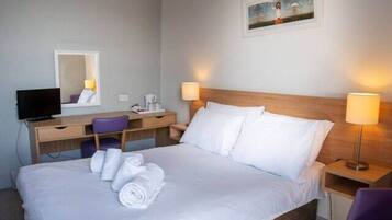 Una habitación de hotel con una cama, un escritorio, una silla, un televisor y dos lámparas de noche.