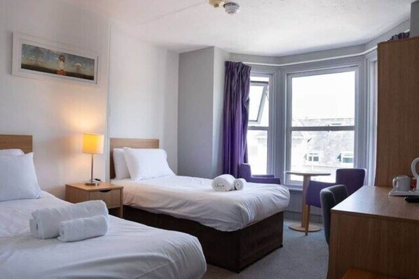 Une chambre d’hôtel avec deux lits, un bureau, une chaise et une fenêtre avec des rideaux.